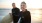 man and woman in wetsuits and holding surfboards at the beach